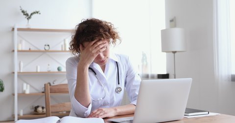 Stressed young female therapist feeling under pressure, worrying about professional mistake, working on computer at workplace. Overworked physician regrets wrong diagnosis or received bad news email.