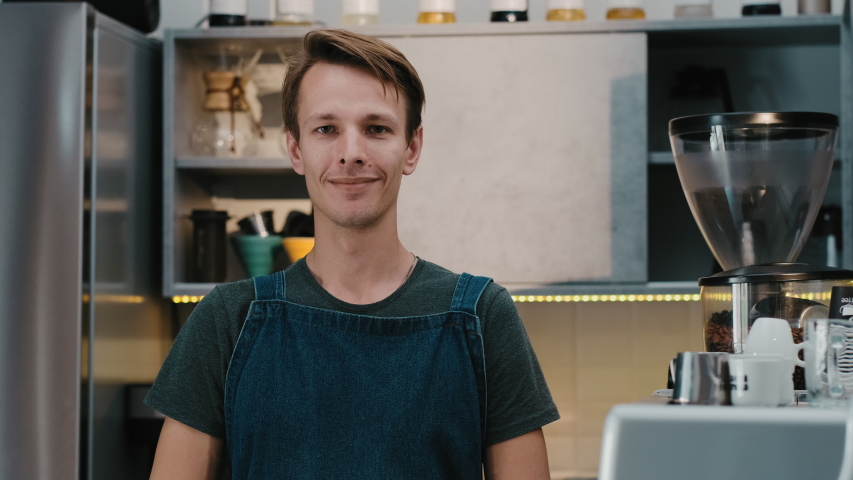 Portrait young man barista happy smiling face looking at camera in coffee shop. Small business owner standing  in uniform with apron.
 | Shutterstock HD Video #1054815494