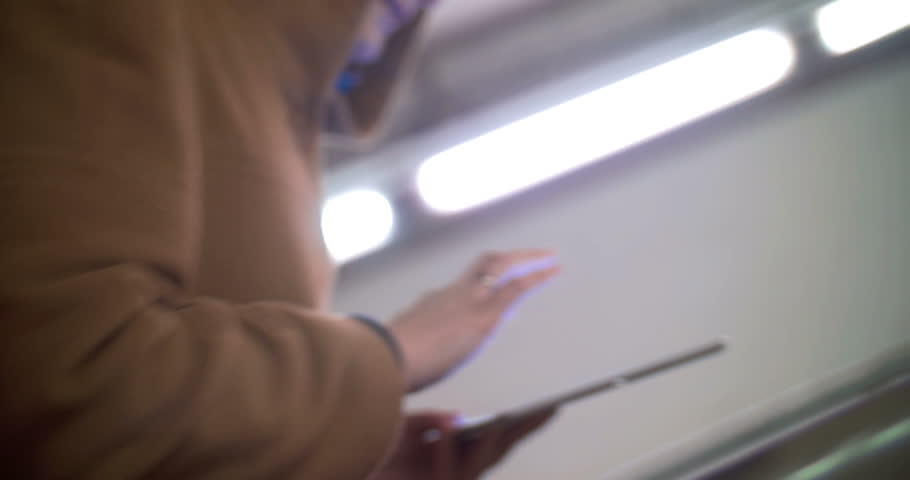 Woman in coat walking fast upstairs in underground and using tablet computer