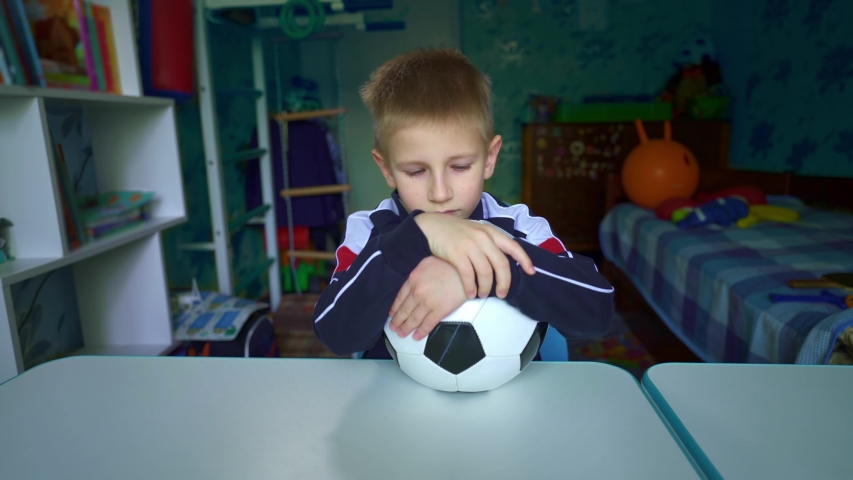 The boy dreams of becoming a great football player.An upset child looks out the window during quarantine. The boy dreams of playing soccer with friends. Longing for the game in the stadium. Lockdown. Royalty-Free Stock Footage #1054819772