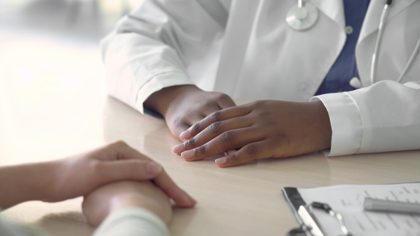African female doctor holding hand supporting caucasian woman patient. Kind ethnic professional physician give empathy concept encourage reassure infertile patient at medical visit, close up view. Royalty-Free Stock Footage #1054823156