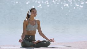 Happy young woman meditating at the seacoast. Girl practicing yoga on the beach at sunrise. Shallow DOF copy space sea background. Music for meditation creative concept - Powered by Shutterstock - Get 15% off with code: PIKWIZARD15