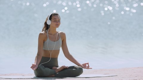 Happy young woman meditating at the seacoast. Girl practicing yoga on the beach at sunrise. Shallow DOF copy space sea background. Music for meditation creative concept