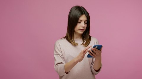 Lovely brunette young woman scrolling internet blog on smartphone, watching photos on social network and expressing amazement, using mobile application. indoor studio shot isolated on pink background