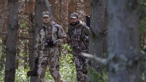 Two hunter men in camouflage clothes with guns walking through forest during hunting season. Man hunter outdoor in forest hunting. Male Tourists. Slow motion