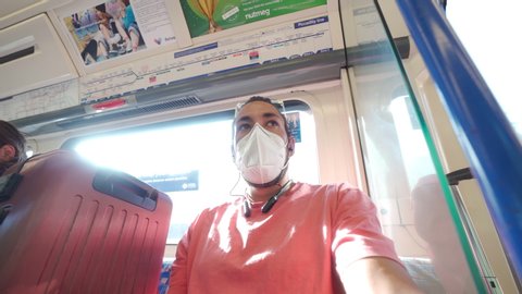 LONDON, ENGLAND - JUNE 16,2020: Person on Piccadilly Line London Underground Train wearing face mask during COVID 19 coronavirus pandemic going at Heathrow airport to travel with luggage