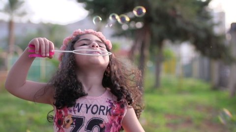 A little cute girl blowing soap bubbles in a park, slow motion