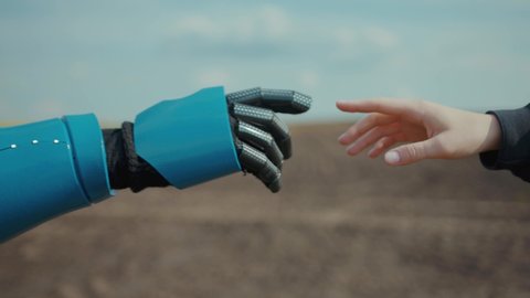 Robot and human pulling hands to reach out each other. Almost reaching robotic cyborg and woman hands outdoors at agricultural field. Human interaction with AI. Future concept.