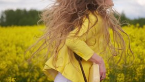 Manual movement of the camera following the dancing guitar player. A beautiful girl in a yellow jacket plays a guitar in a field of rapeseed.