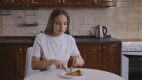 Girl cuts a pizza with a knife and eats it in the kitchen