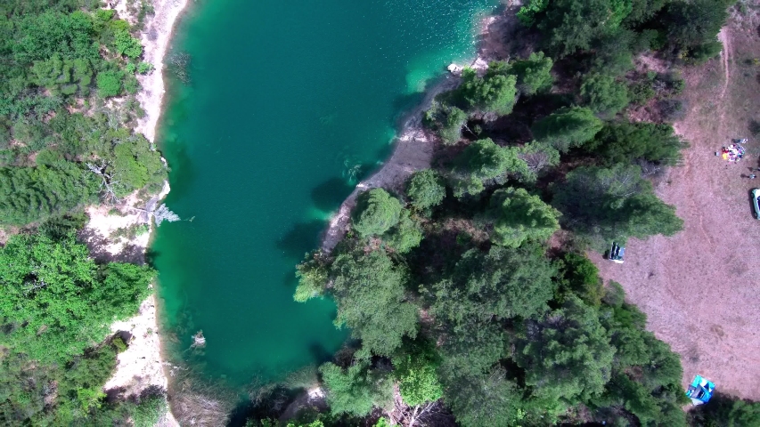 Epic motion lapse lift off above lake Tsivlou in Greece. Green waters surrounded by pine trees and clouds casting moving shadows. Bird-eye view shot.