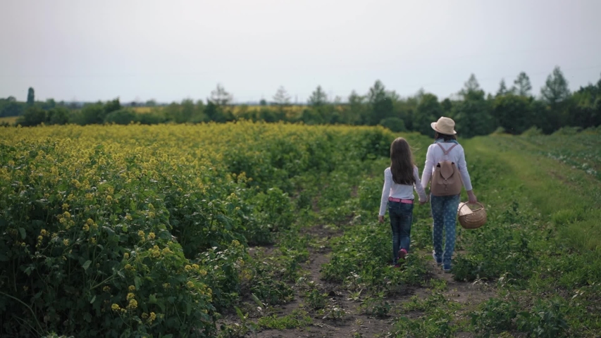 Two girls walk with a basket near a rapeseed field