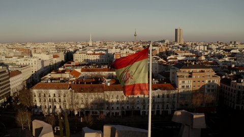 Madrid, Spain. City panorama at sunset, buildings, streets and roofs of houses, view from the top. in the center of the frame the flag of spain soars in the wind