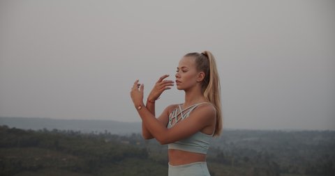 Half-body portrait shot of a female model with long hair tied up as she moves her hands up and down while doing some stretching and breathing exercises