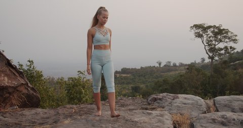 Panoramic shot of a beautiful female model walking barefoot by the rocks on the mountaintop