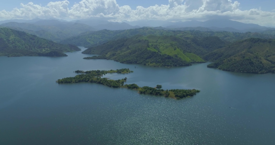 Beautiful lake by green hillside forest with Cordillera Central (Hispaniola) mountain range in background, Dominican Republic, overhead aerial approach Royalty-Free Stock Footage #1054849241