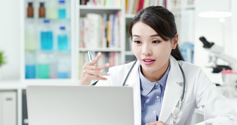 Telemedicine concept - asian female doctor listening to patient talking symptom on the internet and she write down notes