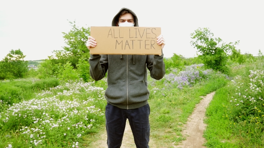 Young man in a mask with a cardboard poster in his hands with the inscription - ALL LIFES MATTER. One protest