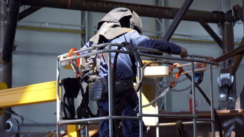 Professional heavy industry worker welder in protective mask and suit works with metal construction on factory. Steel and iron welding construction site. Welding equipment preparation for work. 