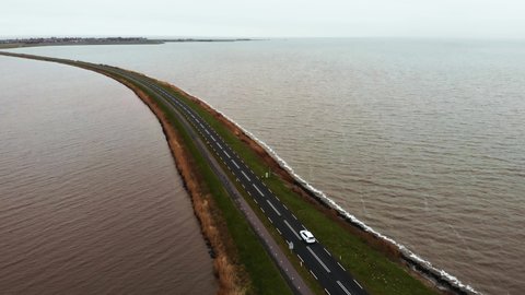 Aerial Flyby shot of White car moving by the Highway Road on the Dam in Netherlands connecting Mainland with a Marken island in Holland