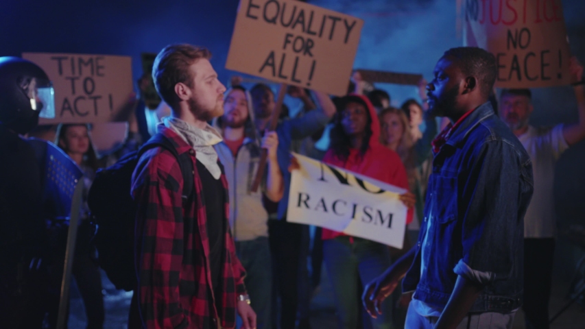 Caucasian and afro-american men shaking hands in agreement at street riot. Multi-cultural young friendly people protest for human equality. End of conflict. Friendship. Royalty-Free Stock Footage #1054857596