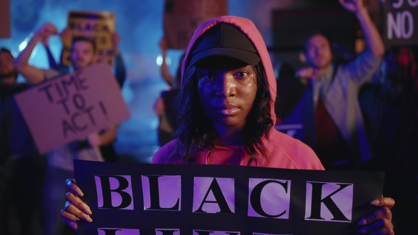 Confident black woman holds invocatory poster, standing in crowd of shouting activists, protesting for equal rights and black lives matter. Solidarity demonstration. Royalty-Free Stock Footage #1054857728