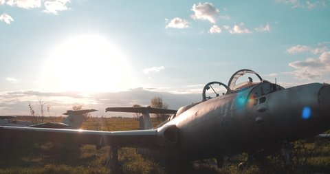 Close-up view of pair of Soviet military fighter planes from World War 2 on field against the backdrop of bright big sun and clouds in the summer. Broken bomber aircraft in the old abandoned airfield.