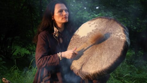 Shaman woman playing on shaman frame drum in the nature
