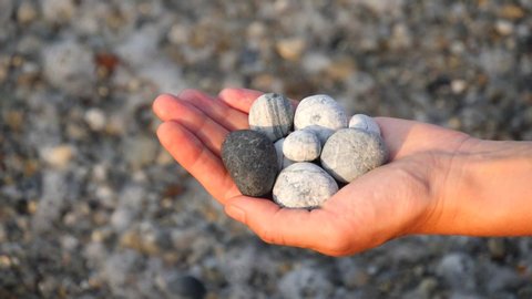 Blurry defocus Beautiful round gray, white sea stones lie in a female hand against background of beach, coast with sea stones, sea waves and foam. Concept of relaxation, meditation. Slow motion video.