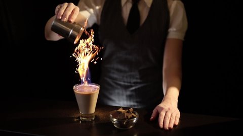 Bartender serving Baileys comet cocktail, sprinkling cinnamon powder over a burning cocktail causing beautiful sparkling effect; Irish cream cocktail on fire