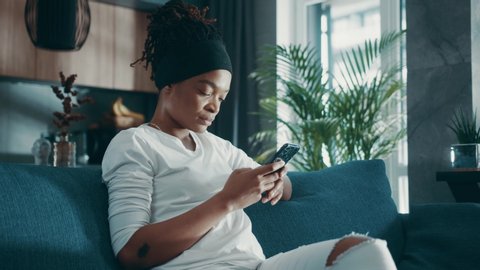Close up relaxed afro american woman hold use smart phone watching social media sit on sofa technology young smartphone shopping online sale slow motion
