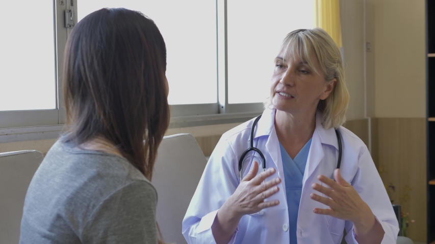 Senior female doctor in uniform is sitting to talking with a female patient who came to see the doctor in the health care center. | Shutterstock HD Video #1054864175