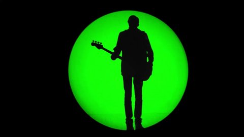 Shadow of an unrecognizable bassist in a round beam of green light. Musician playing a bass guitar