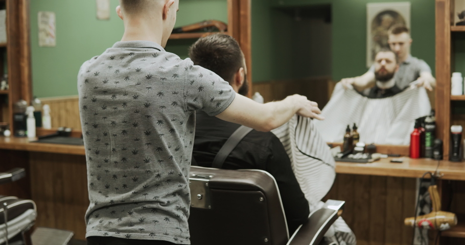 Close-up of barber cuts the hair by scissors at barbershop. Hairdresser's hands at working process. Barber making haircut of attractive bearded man in barbershop. Hairdresser at work. Beauty saloon. | Shutterstock HD Video #1054868039