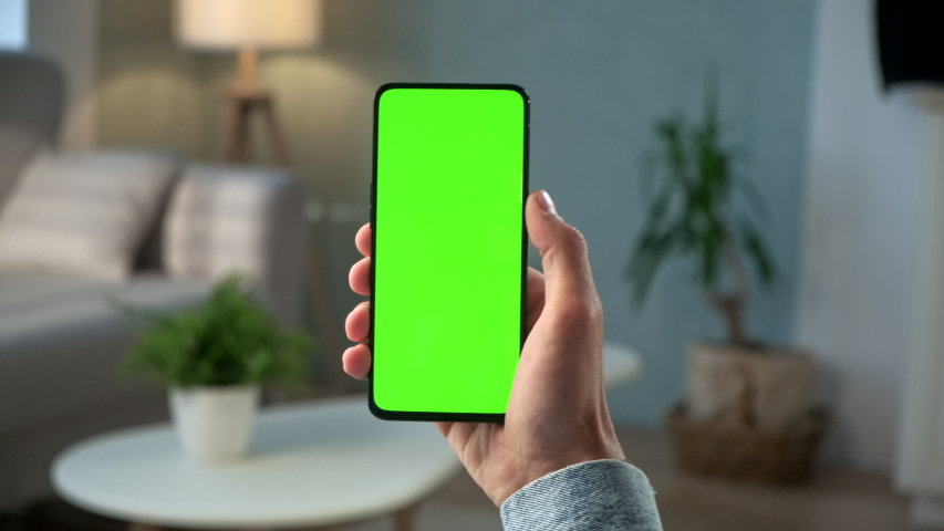 Handheld Camera: Young Man at Home Holding Chroma Key Green Screen Smartphone Watching Content Without Touching or Swiping. Boy Using Mobile Phone, Browsing Internet, Watching Content, Videos,.POV Royalty-Free Stock Footage #1054870505