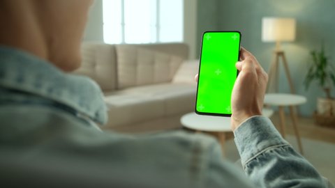 Back View of Brunette Man Holding Chroma Key Green Screen Smartphone Watching Content Without Touching or Swiping. Boy Using Mobile Phone, Browsing Internet, Watching Content, Videos, Blogs.