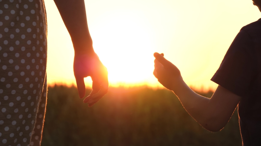 A little boy takes his mother's hand in the background of the sunset. The sun's rays pass through your fingers. Family value. Close-up. | Shutterstock HD Video #1054872158