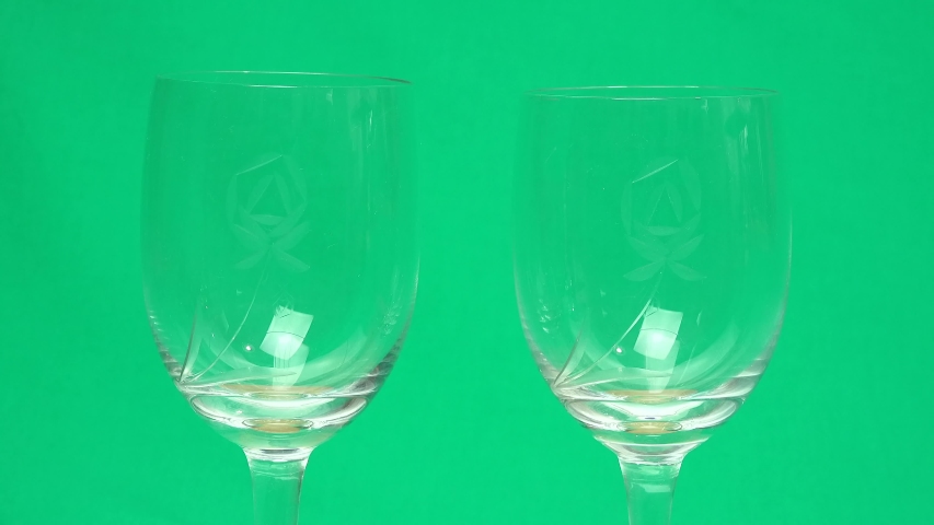 Filling two glasses (with a rose engraving) with champagne pouring from a bottle on a green screen background