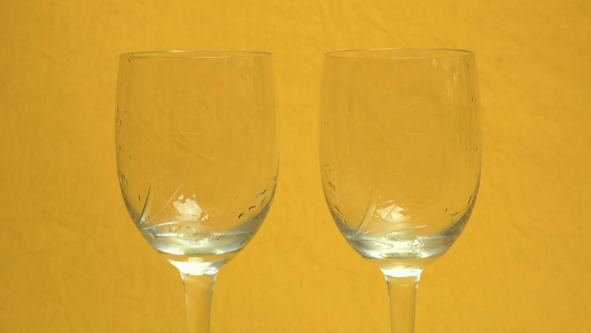 Filling two glasses (with a rose engraving) with champagne poured from a bottle, on an orange background and with a slight zoom in