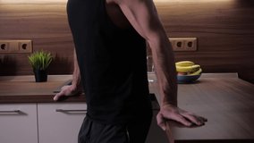 A young man with large biceps in a black t-shirt exercises in isolation using a kitchen set for push ups instead of bars