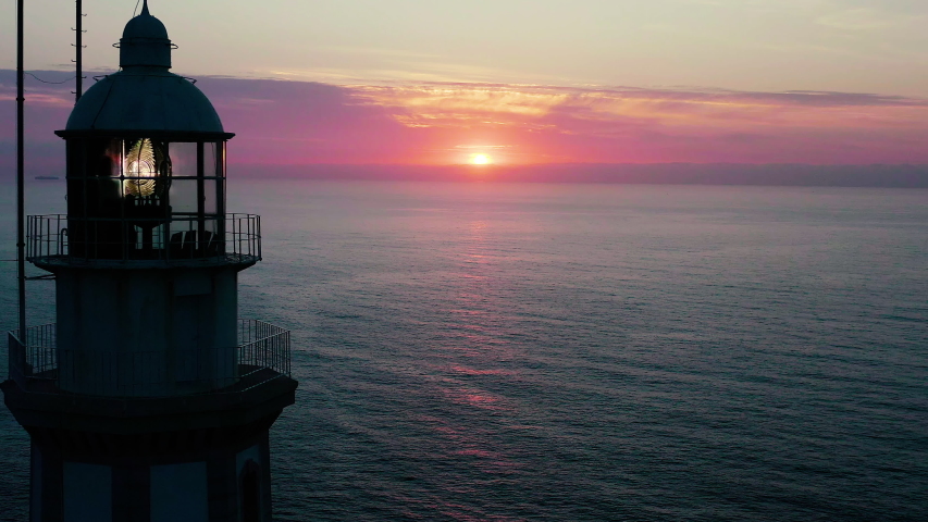 Aerial view of beautiful sunrise behing the dome and light of the lighthouse of the Cape La Nao in Javea, Spain. Royalty-Free Stock Footage #1054879550