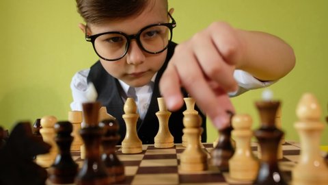 Child playing chess at table. Little boy with glasses developing chess strategy, play board game with friend.