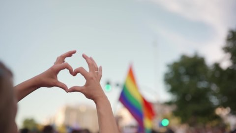 Gay pride lgbt flag Supporting hands make heart sign and wave in front of a rainbow flag flying on the sidelines of a summer gay pride parade	