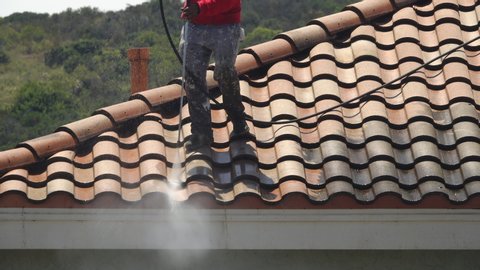 Medium shot of a worker pressure-washing a tile roof