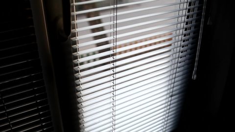 The male hand rotates the handle to close the horizontal blinds, blocking the light from the street. Window blinds open and close.