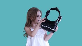 Small schoolgirl wearing Virtual reality helmet is fearful after the game, expresses dislike at studio on blue background. VR concept. Children and modern technology concept. - Powered by Shutterstock - Get 15% off with code: PIKWIZARD15