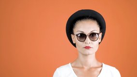 Omg! Studio shot of shocked  woman with sun glasses and stylish hat. Portrait of shocked brunnet stylish girl. Isolated over orange background, free space for your promotion. 