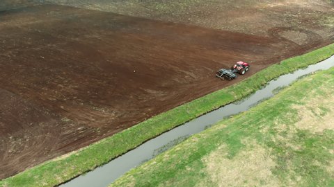Aerial: a farmer on a modern tractor cultivates farmland with a disc harrow near a small reclamation river. Concept of agribusiness. Problem of water pollution and siltation by agricultural production