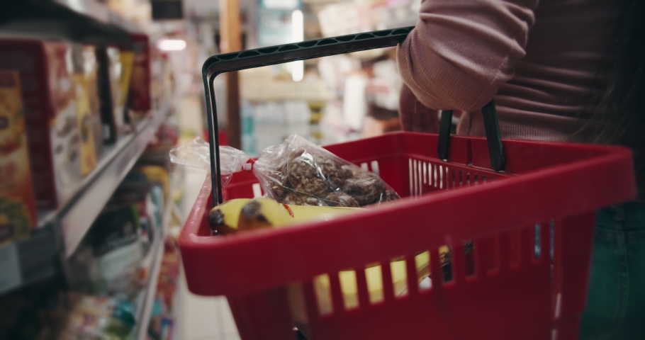 Close up of female customer carrying on red basket full of high quality products at grocery store. Happy woman doing regular shopping of goods at local market Royalty-Free Stock Footage #1054902635