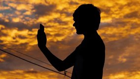 Silhouette of a kid talking on mobile phone in front of sky during sunset	
